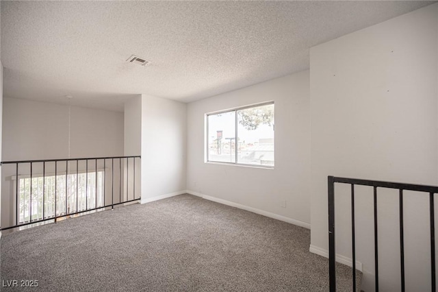 spare room featuring carpet, visible vents, baseboards, and a textured ceiling