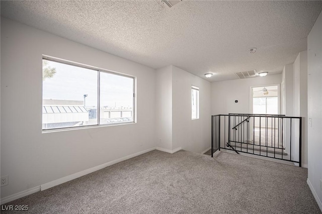 spare room with carpet, visible vents, a textured ceiling, and baseboards