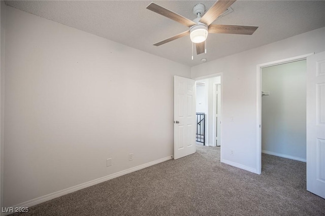 unfurnished bedroom with baseboards, ceiling fan, carpet, a spacious closet, and a textured ceiling