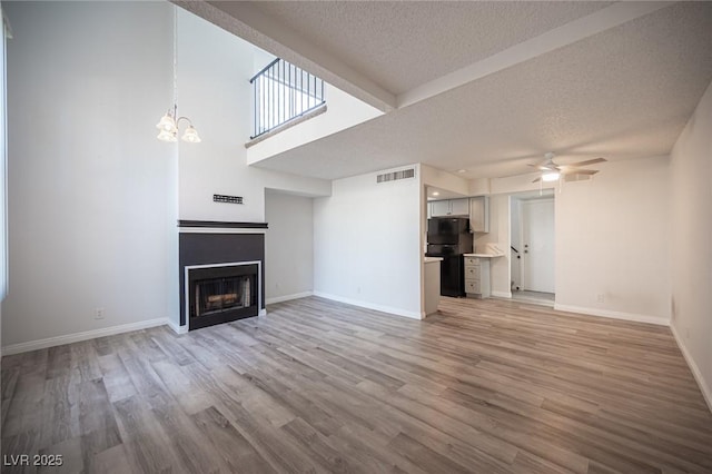 unfurnished living room with a fireplace, light wood-style flooring, a textured ceiling, baseboards, and ceiling fan with notable chandelier