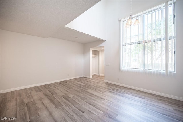 unfurnished room featuring a chandelier, a textured ceiling, baseboards, and wood finished floors