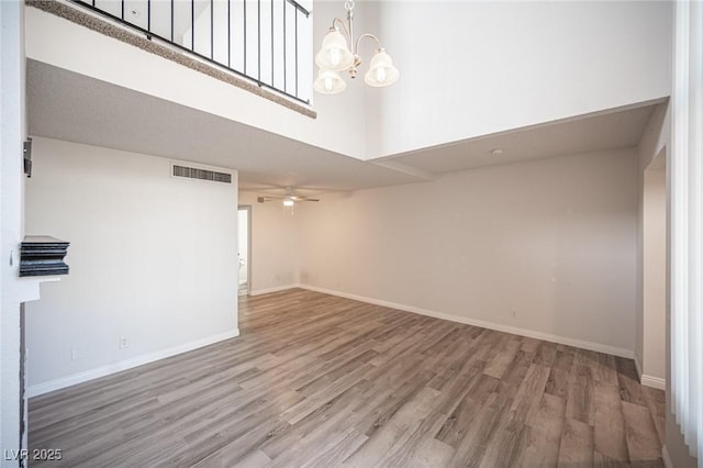 empty room featuring visible vents, a towering ceiling, wood finished floors, baseboards, and ceiling fan with notable chandelier