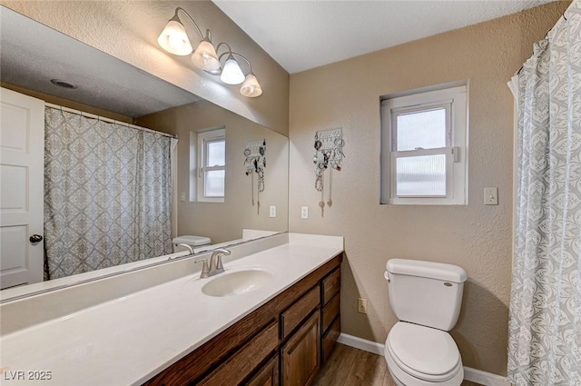 full bath with a textured wall, toilet, vanity, wood finished floors, and baseboards