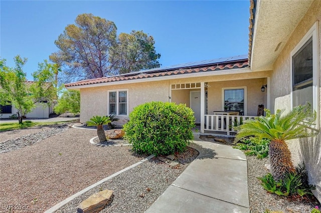 doorway to property with a porch, solar panels, a tiled roof, and stucco siding