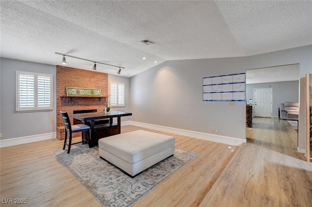 dining space featuring a fireplace, visible vents, vaulted ceiling, light wood-type flooring, and baseboards