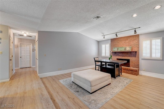 dining area featuring light wood finished floors, lofted ceiling, visible vents, a brick fireplace, and baseboards