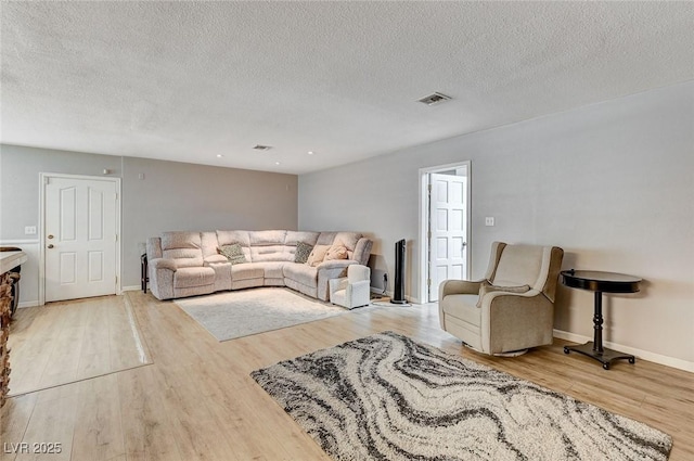 living room featuring a textured ceiling, light wood finished floors, visible vents, and baseboards