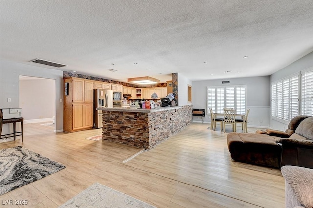 kitchen featuring visible vents, appliances with stainless steel finishes, light brown cabinets, light wood-type flooring, and a peninsula