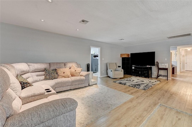 living room featuring baseboards, a textured ceiling, visible vents, and wood finished floors