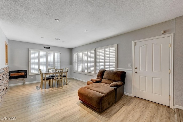 dining space with a textured ceiling, baseboards, visible vents, and light wood-style floors