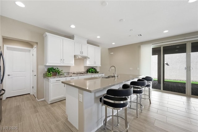 kitchen featuring a breakfast bar, light countertops, white cabinets, a sink, and under cabinet range hood