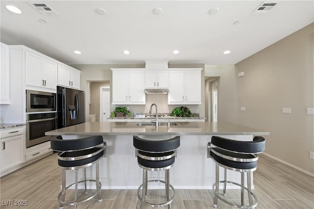 kitchen featuring stainless steel appliances, visible vents, a sink, and an island with sink