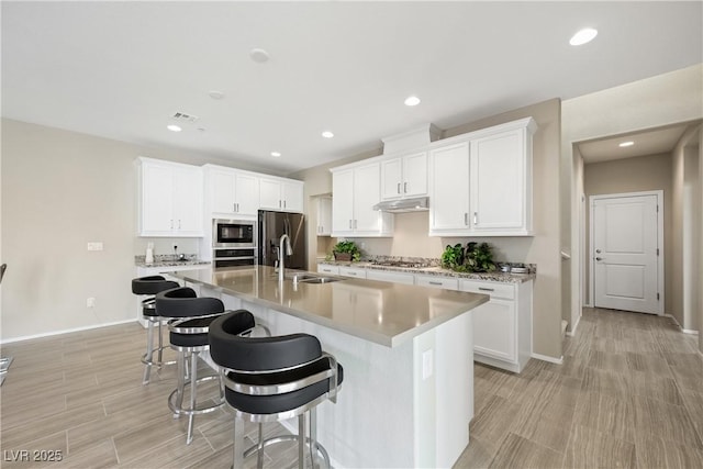 kitchen with appliances with stainless steel finishes, a kitchen island with sink, under cabinet range hood, a kitchen bar, and a sink