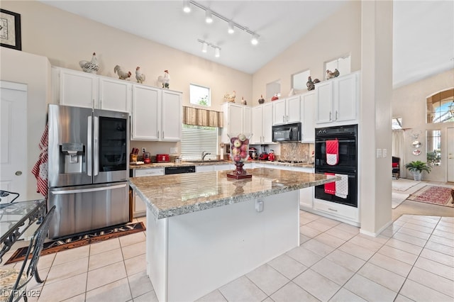 kitchen featuring light tile patterned floors, white cabinets, backsplash, black appliances, and a sink