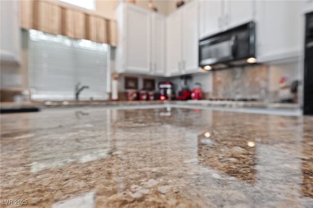 kitchen with light stone counters, black microwave, and white cabinets