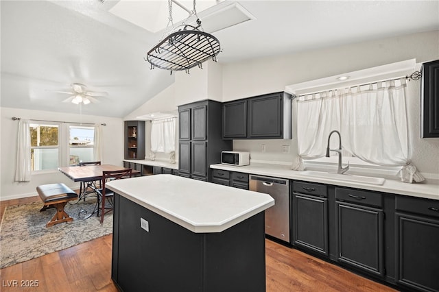 kitchen with white microwave, a sink, vaulted ceiling, stainless steel dishwasher, and a center island