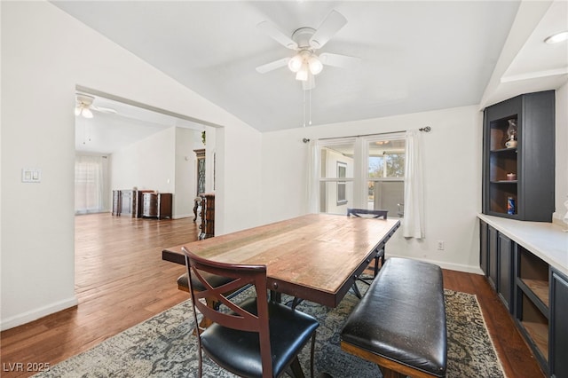 dining space featuring dark wood-style floors, vaulted ceiling, baseboards, and a ceiling fan