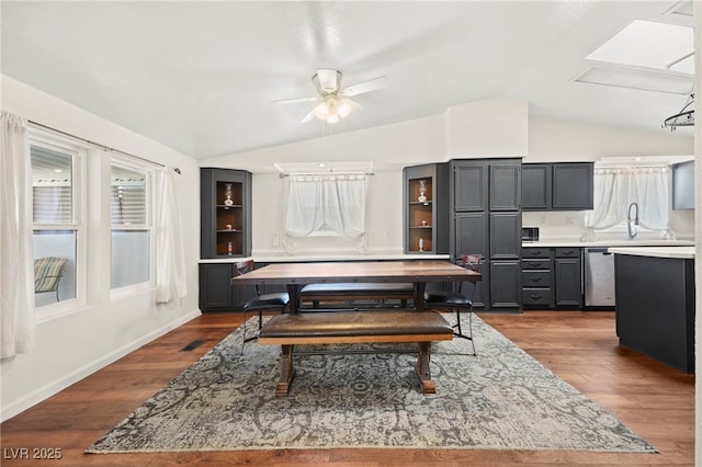 dining room with dark wood finished floors, visible vents, a ceiling fan, vaulted ceiling with skylight, and baseboards