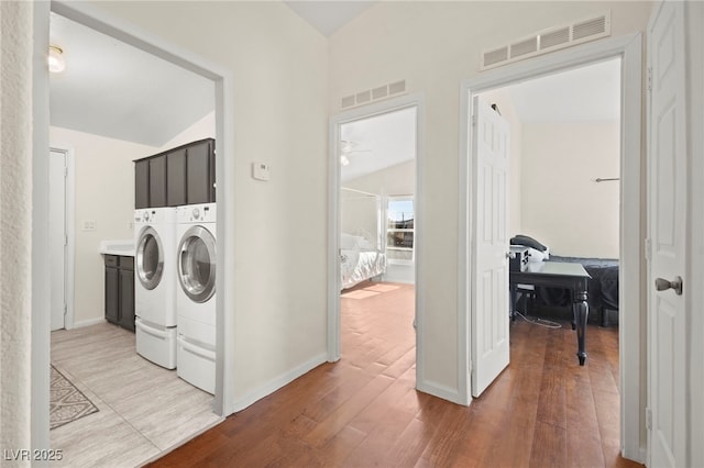 washroom featuring washer and dryer, visible vents, cabinet space, and wood finished floors