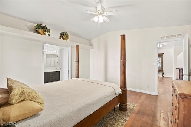 bedroom featuring lofted ceiling, hardwood / wood-style flooring, visible vents, baseboards, and ensuite bath