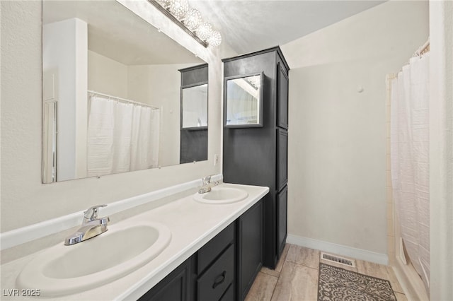 bathroom with double vanity, a sink, visible vents, and baseboards