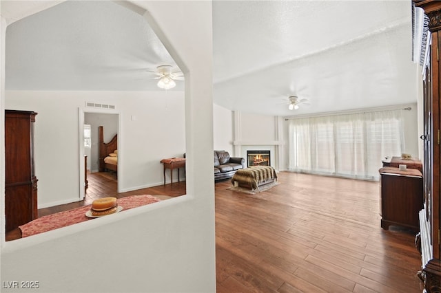 living room featuring a ceiling fan, visible vents, wood finished floors, and a glass covered fireplace