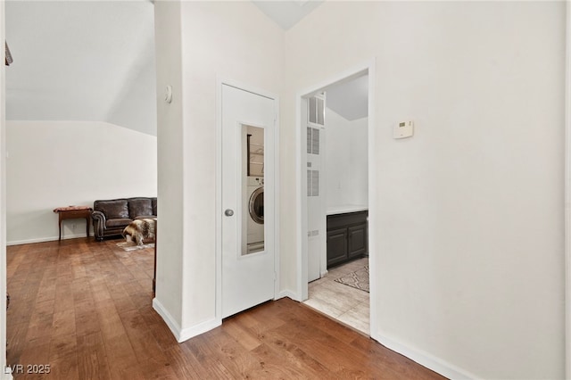 hallway with light wood-type flooring, baseboards, washer / clothes dryer, and lofted ceiling