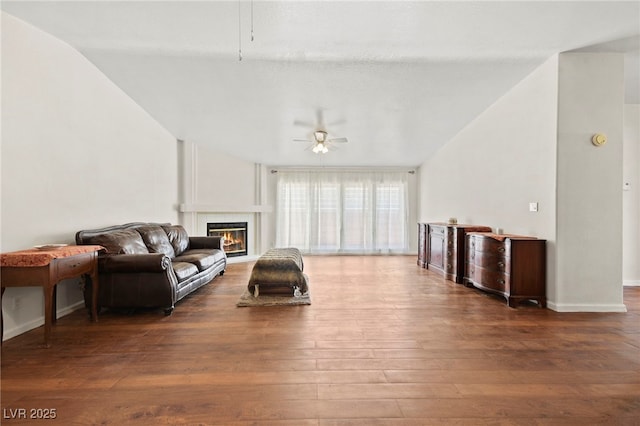 living area with baseboards, a ceiling fan, a glass covered fireplace, wood finished floors, and vaulted ceiling