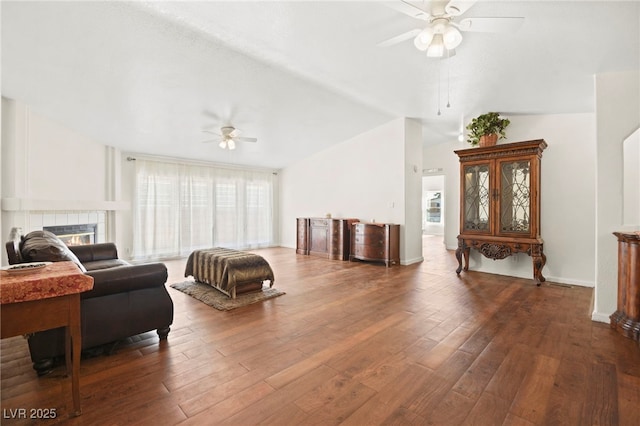 living area with a fireplace, ceiling fan, vaulted ceiling, wood finished floors, and baseboards