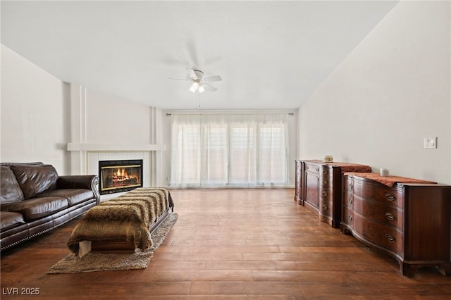 living area with a tile fireplace, dark wood finished floors, and a ceiling fan