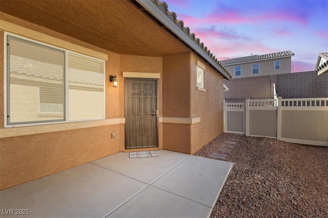 exterior entry at dusk with fence, a patio, and stucco siding