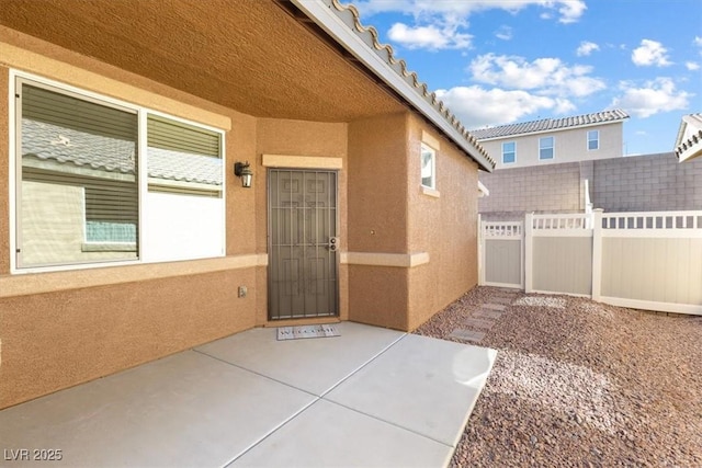 entrance to property with a patio area, fence, and stucco siding