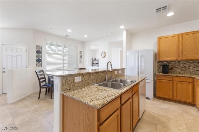 kitchen featuring white appliances, a sink, visible vents, decorative backsplash, and an island with sink