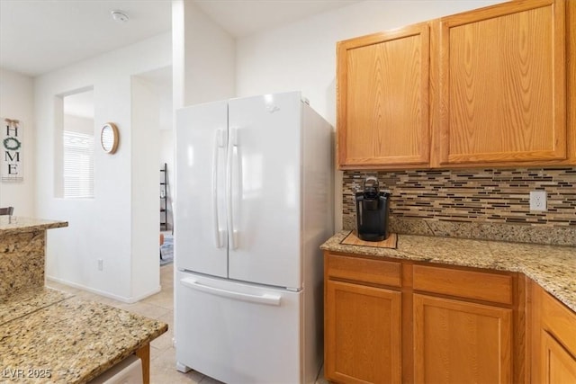 kitchen with light tile patterned floors, backsplash, freestanding refrigerator, light stone countertops, and baseboards