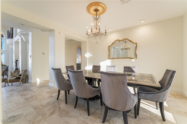 dining room featuring arched walkways, a chandelier, and baseboards