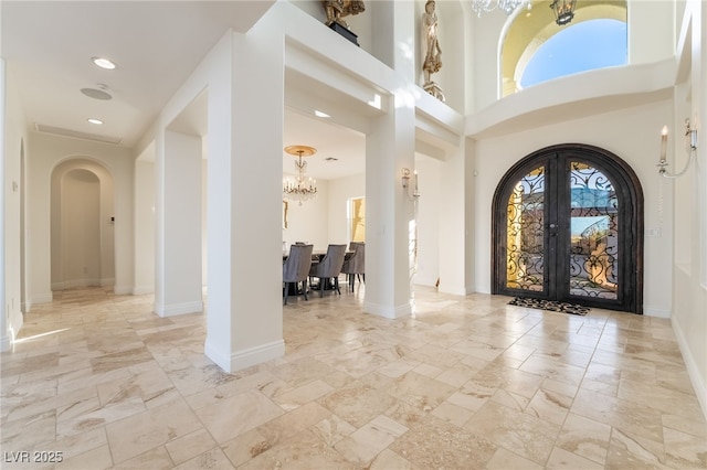 foyer with baseboards, arched walkways, french doors, a chandelier, and recessed lighting