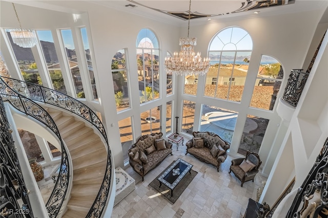 living room with a towering ceiling, an inviting chandelier, stairway, and crown molding