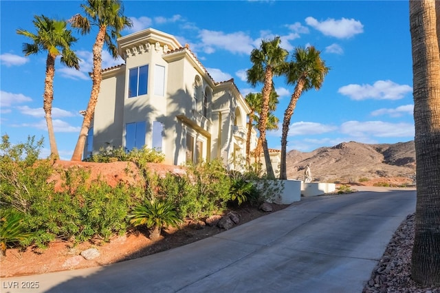 view of property exterior featuring a tiled roof, a mountain view, driveway, and stucco siding