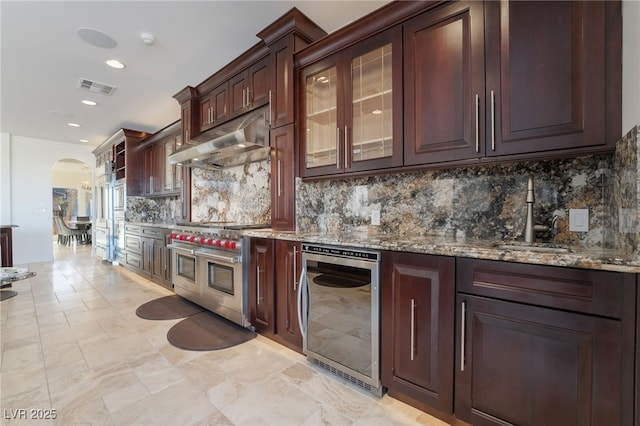 kitchen with range with two ovens, arched walkways, visible vents, beverage cooler, and under cabinet range hood