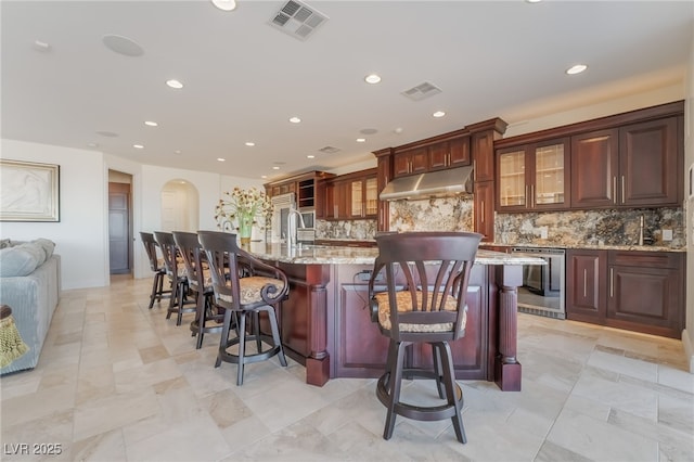 kitchen featuring tasteful backsplash, visible vents, under cabinet range hood, and a spacious island