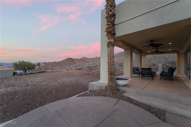 patio terrace at dusk featuring a mountain view and a ceiling fan