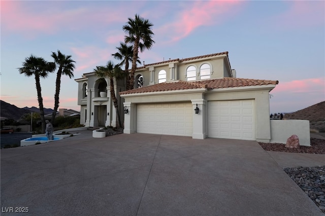 mediterranean / spanish-style home featuring concrete driveway, a tiled roof, an attached garage, and stucco siding