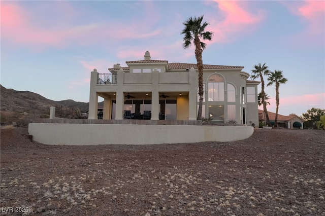 rear view of house featuring a ceiling fan, a balcony, a chimney, a mountain view, and stucco siding