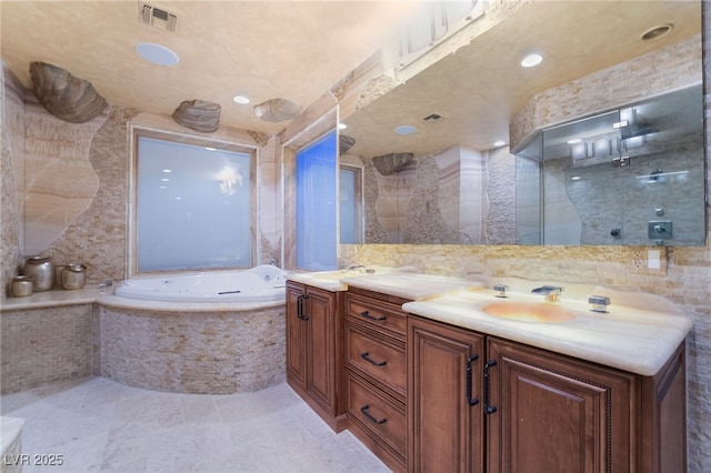 full bathroom featuring double vanity, visible vents, a bath, a sink, and tile walls