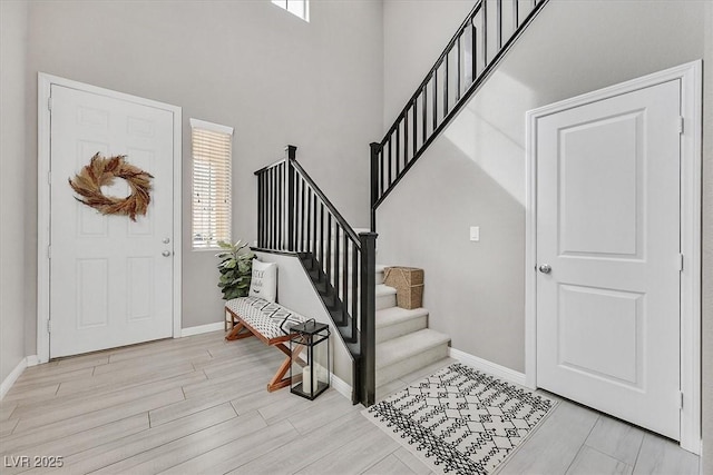 entrance foyer featuring light wood-style floors, a high ceiling, baseboards, and stairs