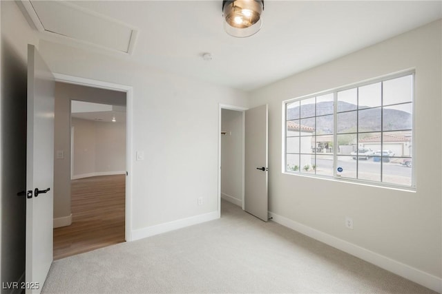 unfurnished bedroom with attic access, baseboards, and light colored carpet