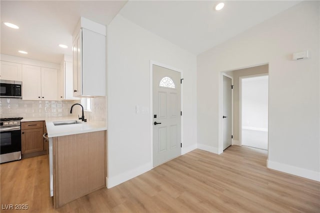 kitchen with light wood-style floors, decorative backsplash, stainless steel appliances, and a sink