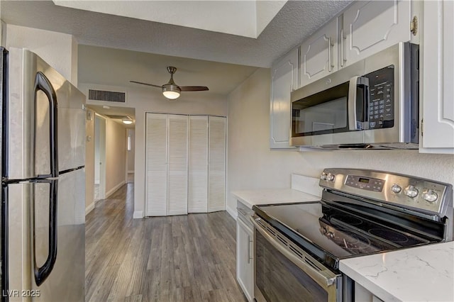 kitchen featuring ceiling fan, stainless steel appliances, wood finished floors, white cabinetry, and baseboards