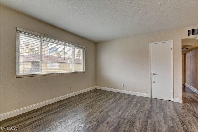 spare room with visible vents, dark wood finished floors, a textured ceiling, and baseboards