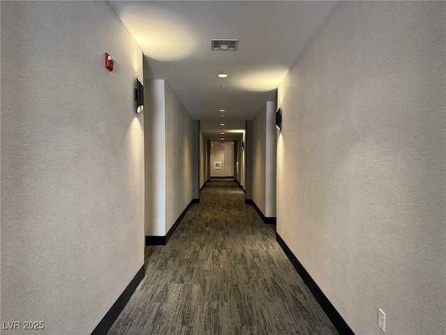 hallway featuring visible vents, a textured wall, and baseboards